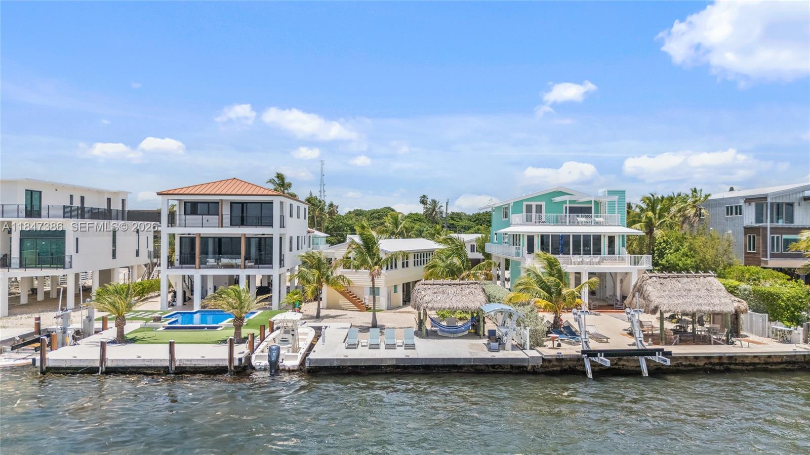 An exterior view shows three waterfront houses with docks, a swimming pool, and palm trees — 235 Tavernier Dr, Key Largo FL 33070, KEY LARGO, FL