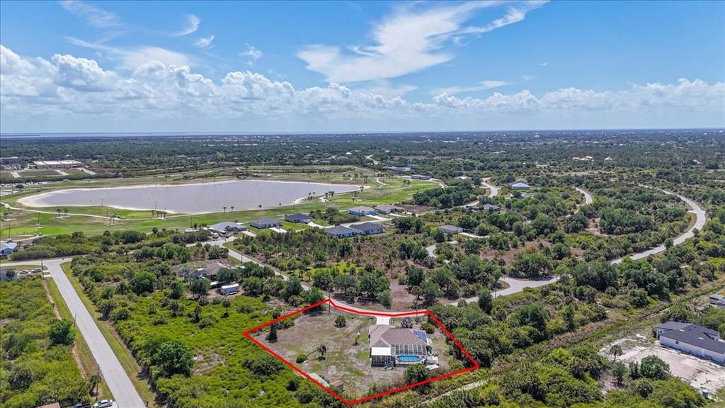 An aerial view shows a house with a pool on a large, partially wooded lot — 6993 MANNIZ ROAD, PORT CHARLOTTE, FL
