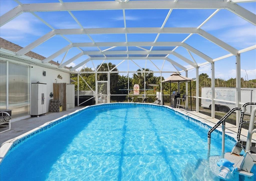 An oval swimming pool is enclosed by a white metal screen structure on a patio — 6993 MANNIZ ROAD, PORT CHARLOTTE, FL