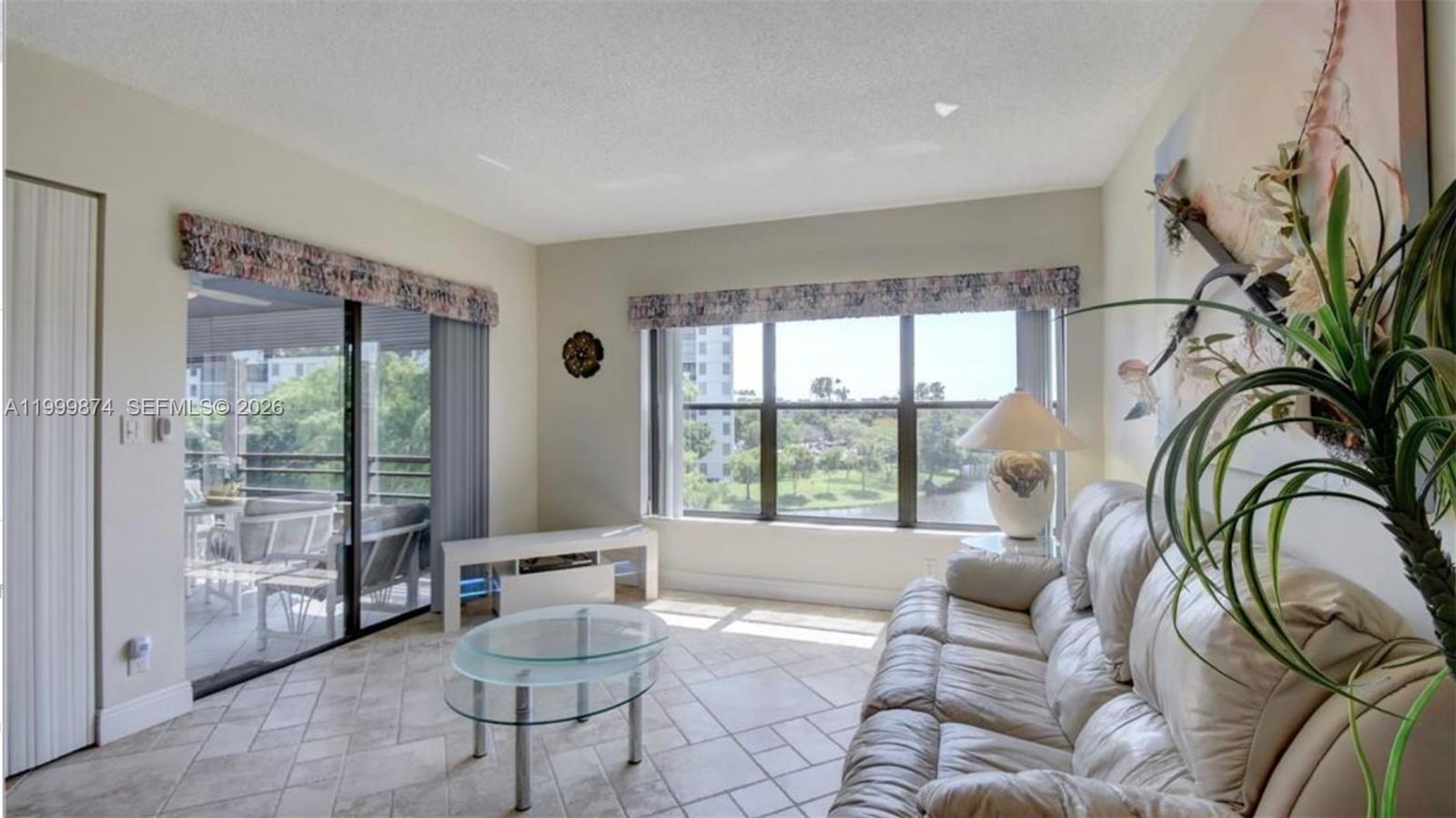 A living room with tile floors, a leather sofa, and a view of a lake — 2311 S Cypress Bend Dr # 419A, Pompano Beach FL 33069, POMPANO BEACH, FL