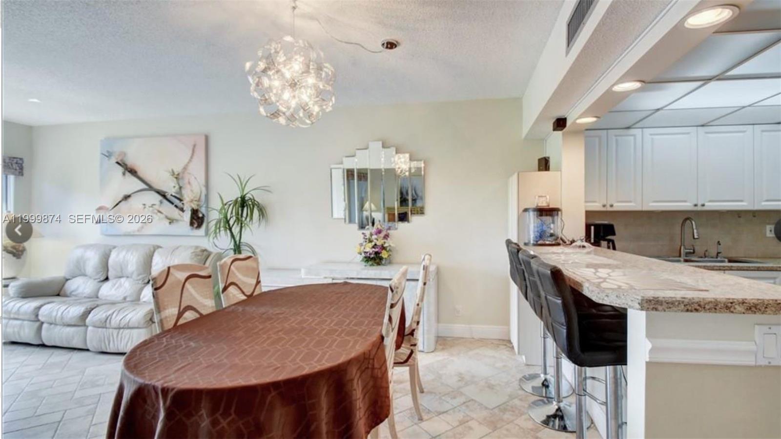 A dining area with a round table, chandelier, and breakfast bar adjacent to a kitchen — 2311 S Cypress Bend Dr # 419A, Pompano Beach FL 33069, POMPANO BEACH, FL