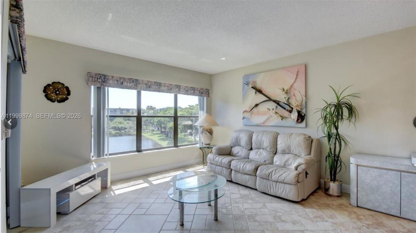 A living room features a white sofa, glass coffee table, tile floors, and a lake view — 2311 S Cypress Bend Dr # 419A, Pompano Beach FL 33069, POMPANO BEACH, FL