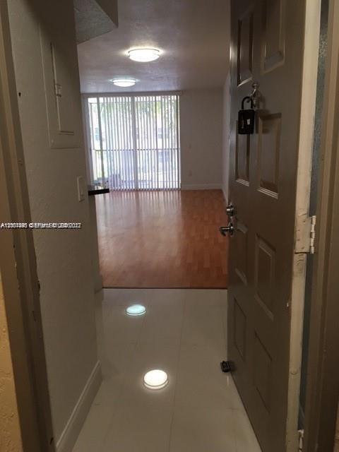 An open door reveals a hallway with white tile floors leading to a wood-floored living area — 8205 Lake Dr # 204, Doral FL 33166, DORAL, FL