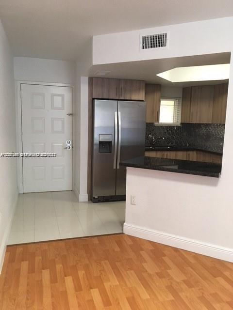 A kitchen with stainless steel appliances, dark countertops, and light wood cabinetry next to an entryway — 8205 Lake Dr # 204, Doral FL 33166, DORAL, FL