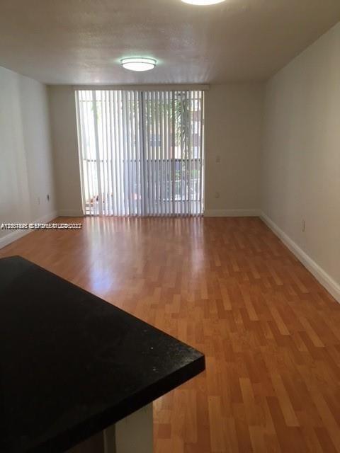 An empty room with light wood flooring, a ceiling light, and vertical blinds over a window — 8205 Lake Dr # 204, Doral FL 33166, DORAL, FL