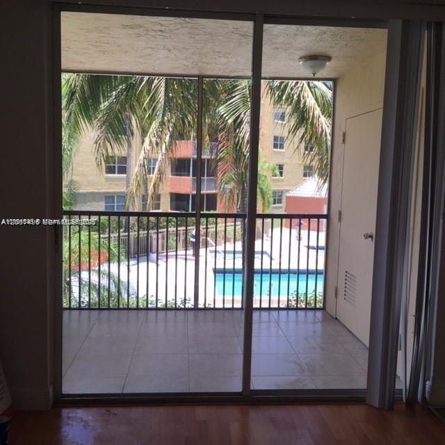 A view from inside through a sliding glass door onto a screened balcony overlooking a pool — 8205 Lake Dr # 204, Doral FL 33166, DORAL, FL