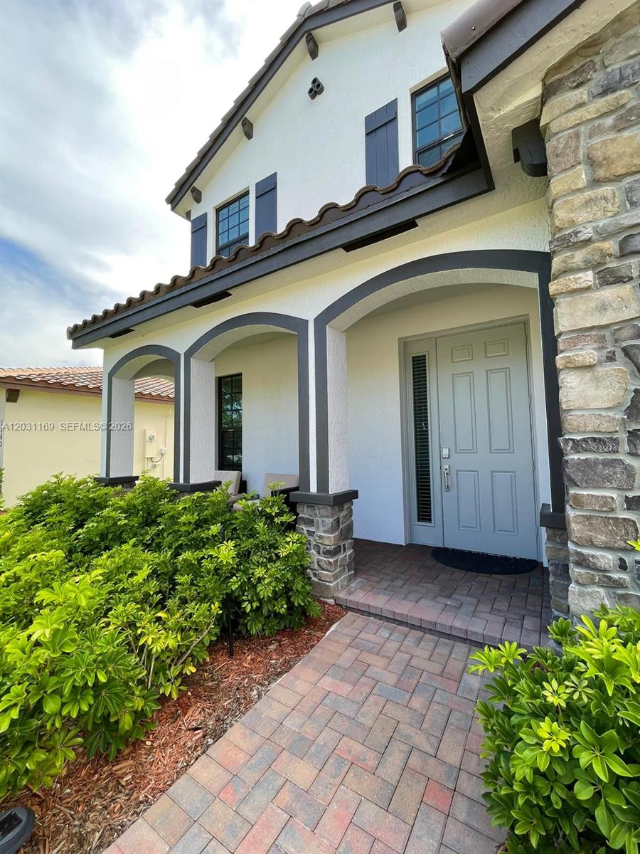 A front exterior view of a house featuring a stone facade, arched entry, and walkway — 3265 Dunning Dr, Royal Palm Beach FL 33411, ROYAL PALM BEACH, FL