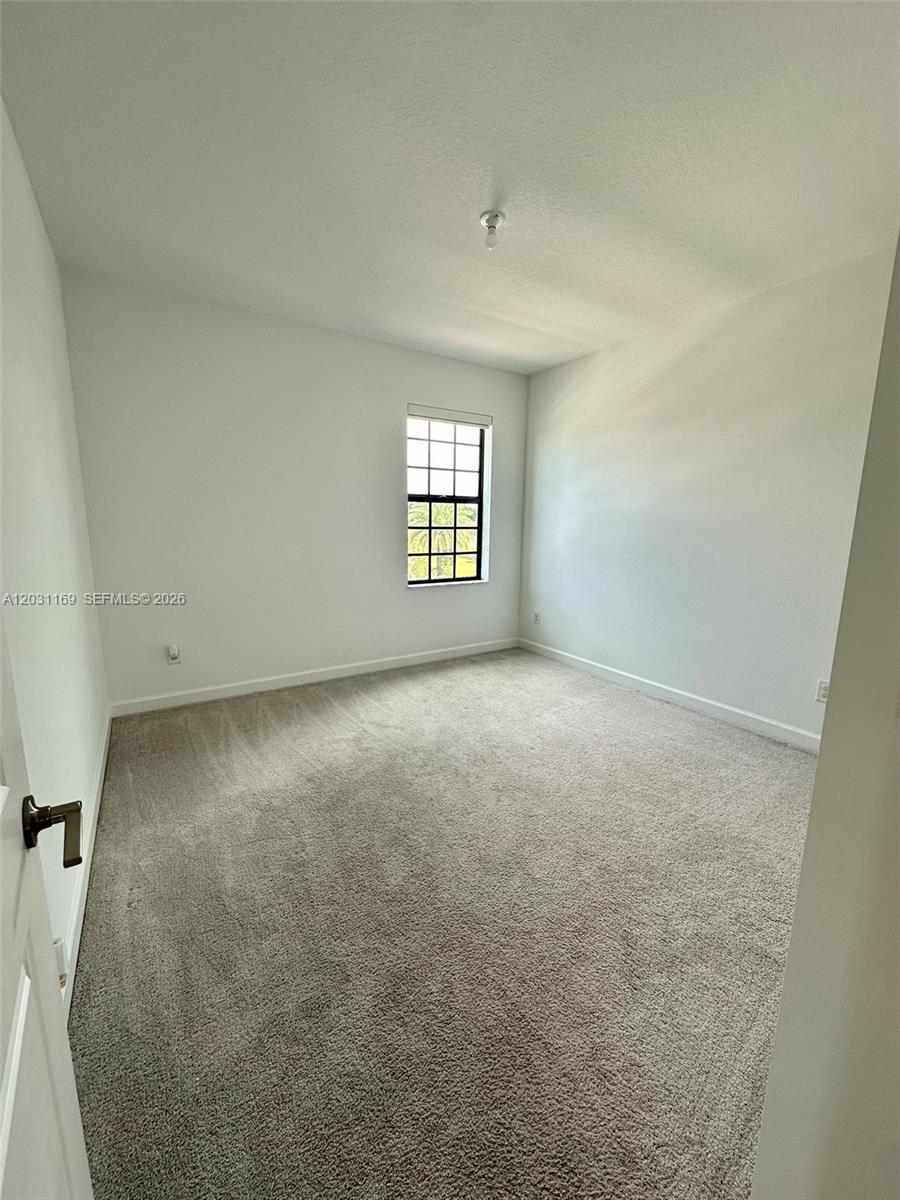 An empty bedroom features white walls, beige carpeting, and a single window with black muntins — 3265 Dunning Dr, Royal Palm Beach FL 33411, ROYAL PALM BEACH, FL