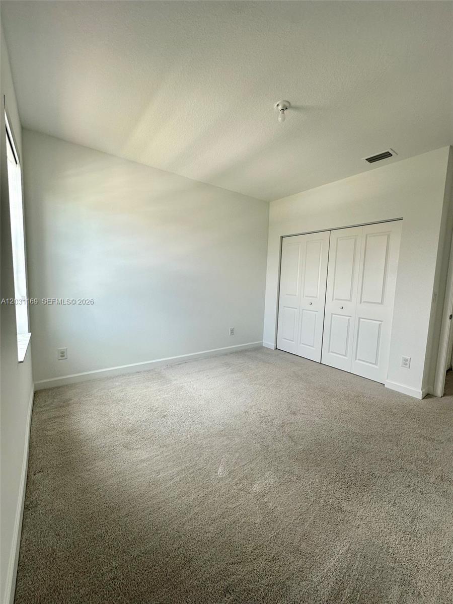 An empty bedroom features beige carpeting, white walls, a window, and a double-door closet — 3265 Dunning Dr, Royal Palm Beach FL 33411, ROYAL PALM BEACH, FL