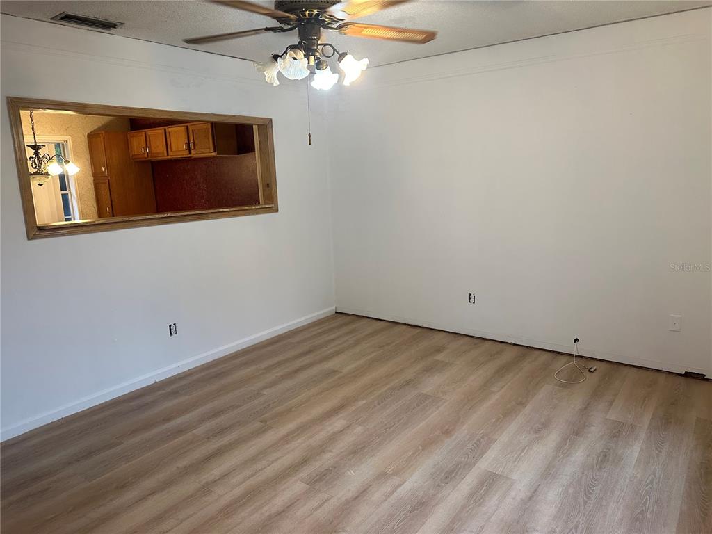 An empty room features light wood-look flooring, white walls, and a large rectangular pass-through window — 1406 MURILLO LOOP, RUSKIN, FL