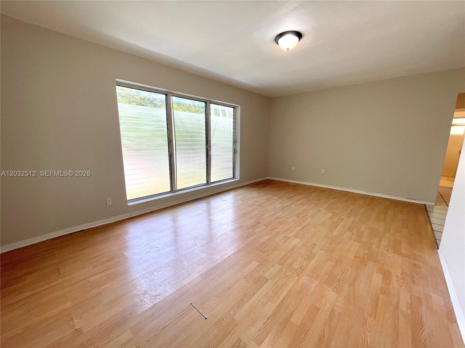 An empty room features light wood flooring, beige walls, and a large three-panel window — 825 Euclid Ave # 9, Miami Beach FL 33139, MIAMI BEACH, FL