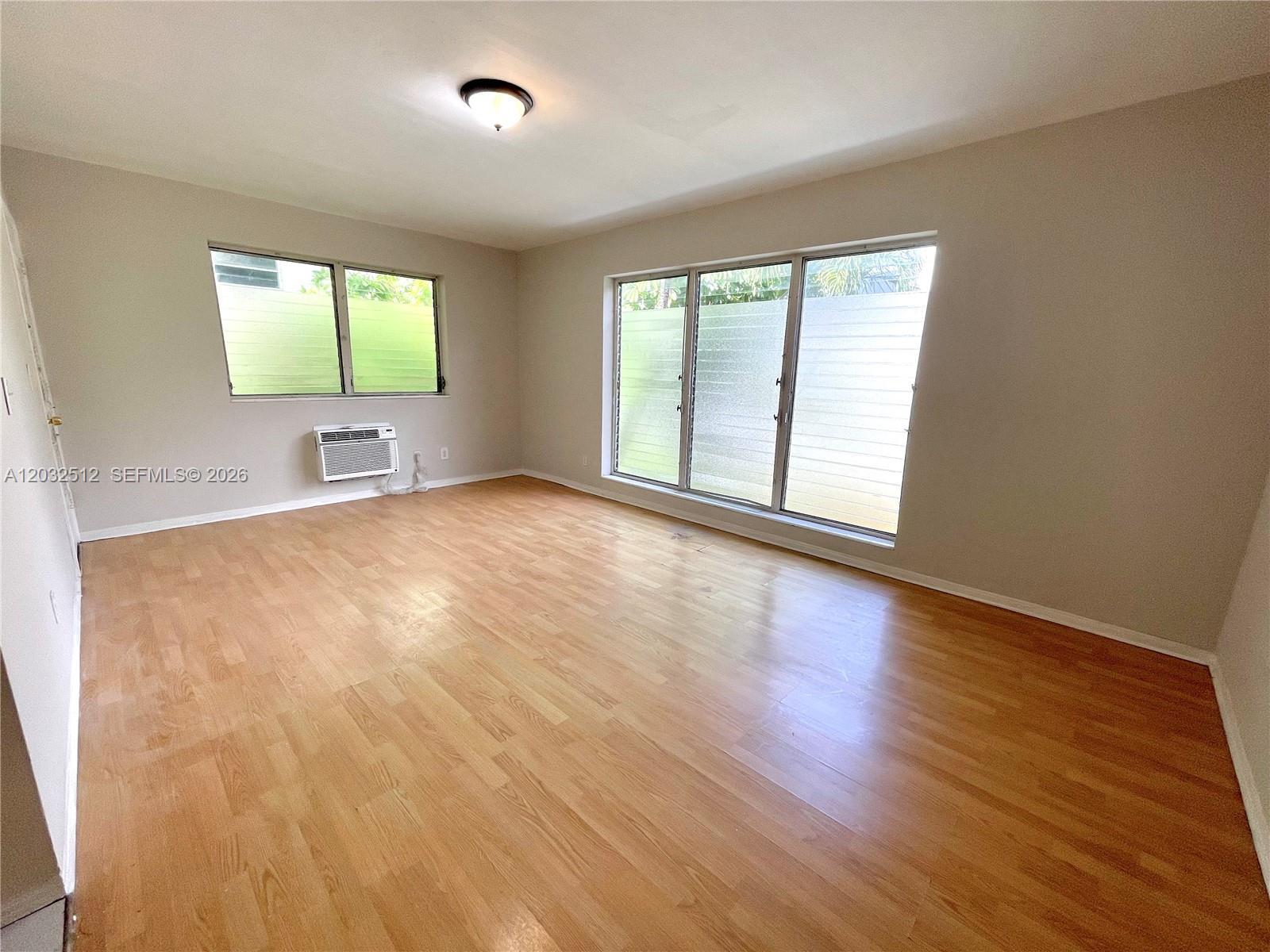 An empty room features light wood laminate flooring, beige walls, and large windows — 825 Euclid Ave # 9, Miami Beach FL 33139, MIAMI BEACH, FL