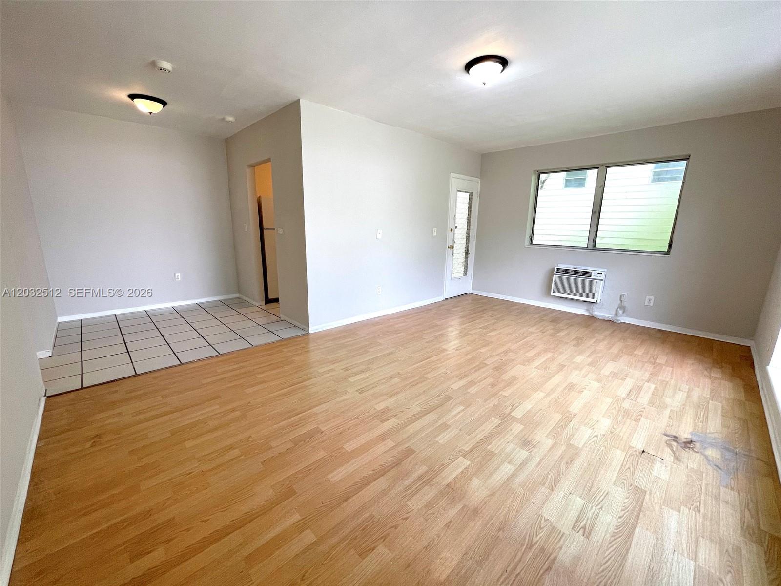An empty room features light wood-look flooring, a tiled corner area, and a window unit — 825 Euclid Ave # 9, Miami Beach FL 33139, MIAMI BEACH, FL