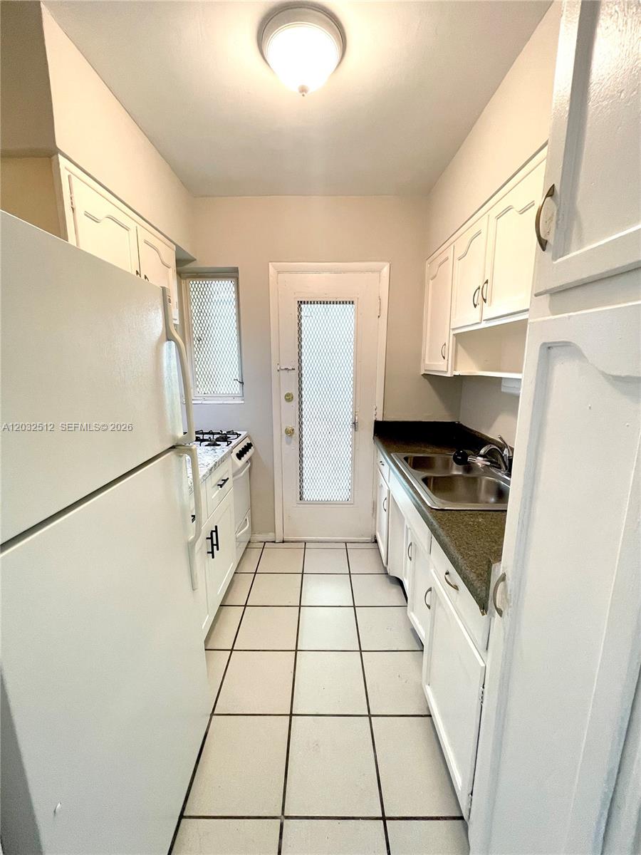 This narrow galley kitchen features white cabinets, dark countertops, and white tile flooring — 825 Euclid Ave # 9, Miami Beach FL 33139, MIAMI BEACH, FL