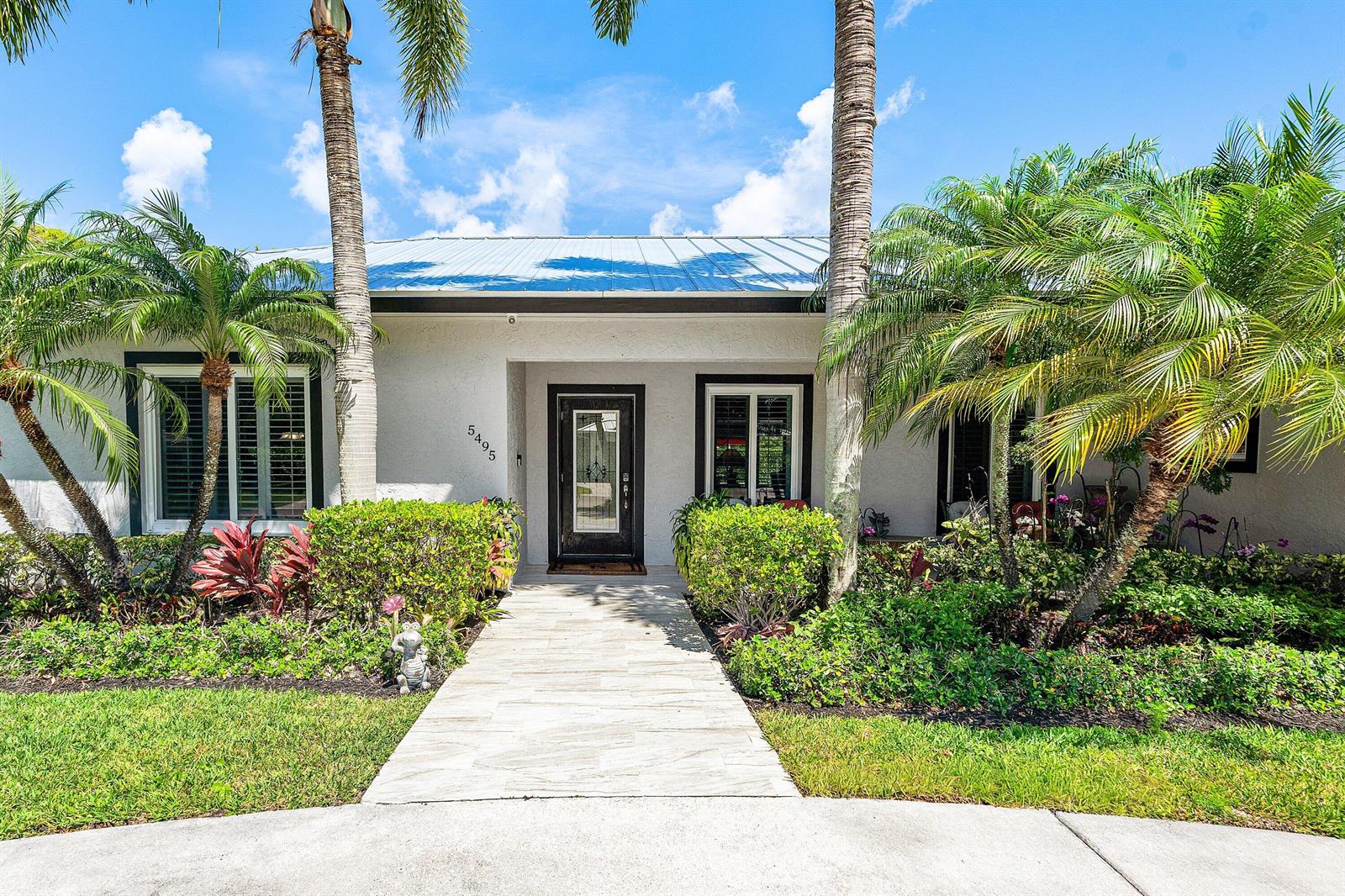 A single-story house with a white stucco facade, metal roof, and a paved front walkway — 5495 Hibiscus Road, Jupiter FL 33458, JUPITER, FL