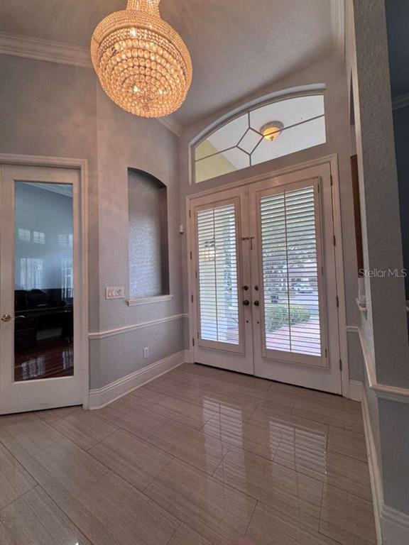 A bright entryway features a crystal chandelier, tiled floors, and double doors with plantation shutters — 7600 DEBEAUBIEN DRIVE, ORLANDO, FL
