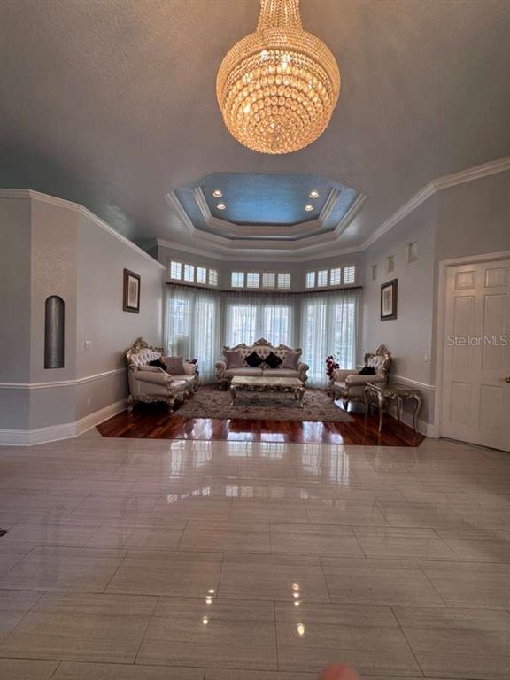 A formal living room features a crystal chandelier, tray ceiling, tile flooring, and ornate furniture — 7600 DEBEAUBIEN DRIVE, ORLANDO, FL