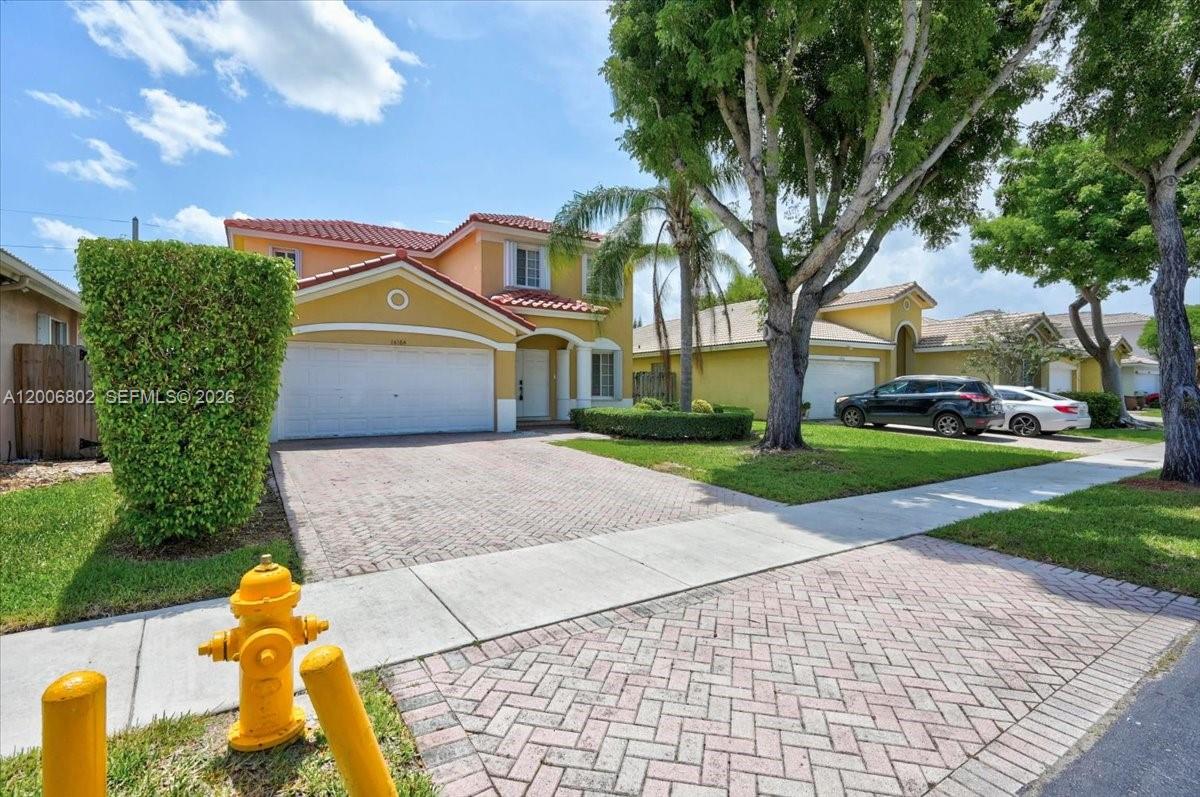 A two-story yellow house with a paved driveway and a fire hydrant in the foreground — 14164 SW 156th Ave, Miami FL 33196, MIAMI, FL