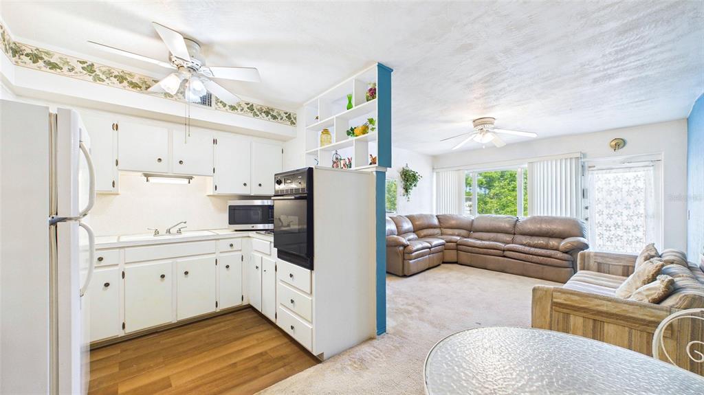 A kitchen with white cabinets and a wall oven opens into a carpeted living area — 5664 40TH TERRACE N UNIT 428, ST PETERSBURG, FL