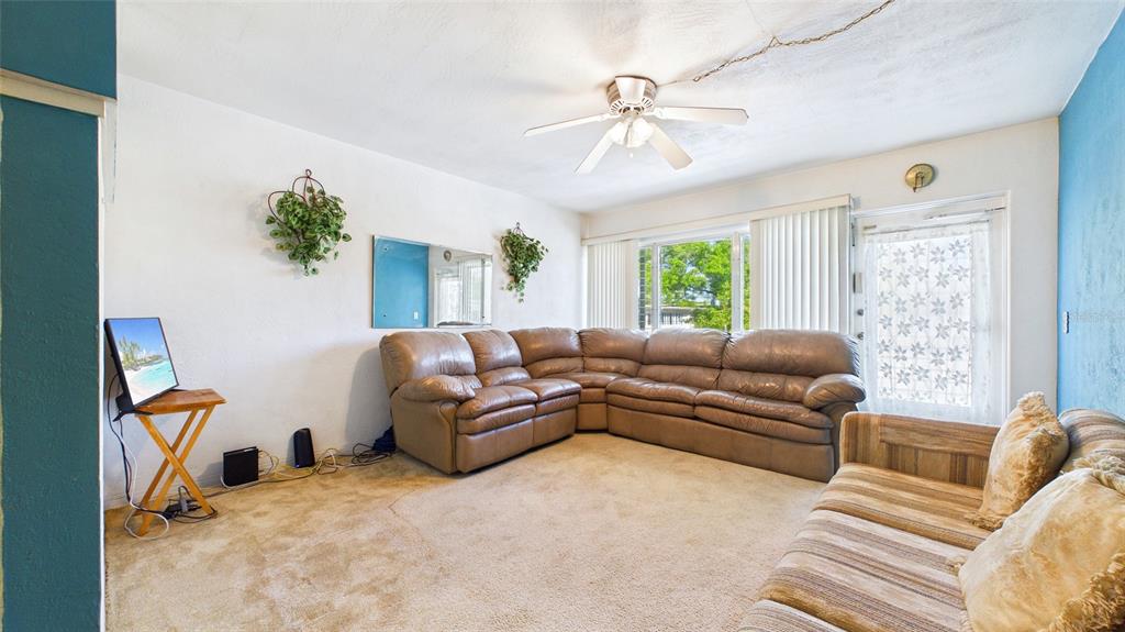 A living room features a large brown sectional sofa, beige carpeting, and a ceiling fan — 5664 40TH TERRACE N UNIT 428, ST PETERSBURG, FL