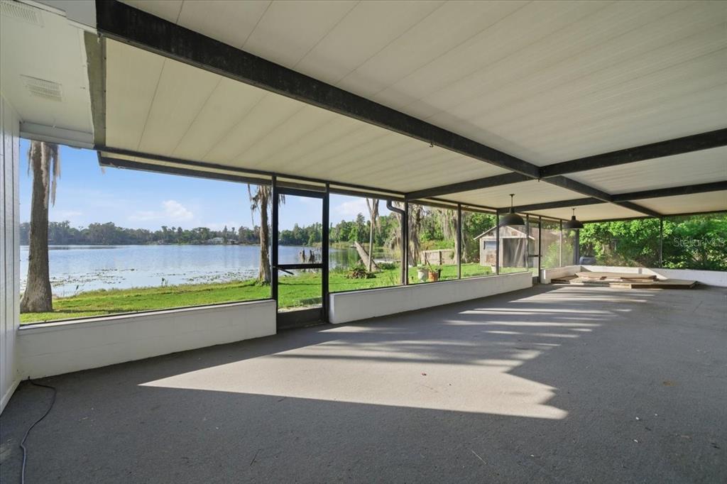 A large, covered concrete patio overlooks a lake with a grassy yard and trees — 700 DRUID WAY, LUTZ, FL