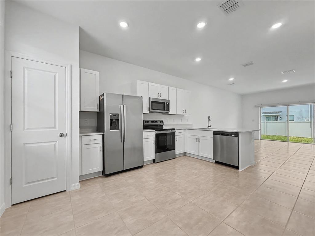 A kitchen features white cabinets, stainless steel appliances, and tile flooring in an open space — 2949 SKYLINE LOOP, KISSIMMEE, FL