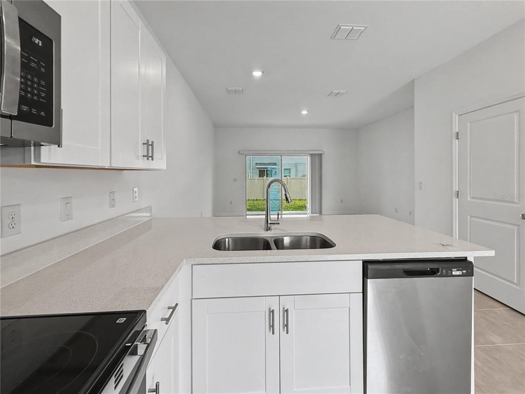 A kitchen with white cabinets, stainless steel appliances, and a sink on a quartz countertop — 2949 SKYLINE LOOP, KISSIMMEE, FL