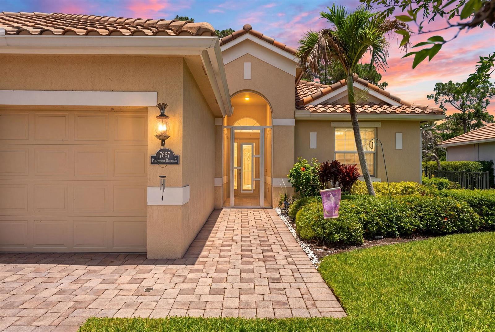A beige house exterior features a paved walkway, a garage, and a screened front entryway — 7657 Fieldstone Ranch Square, Vero Beach FL 32967, VERO BEACH, FL