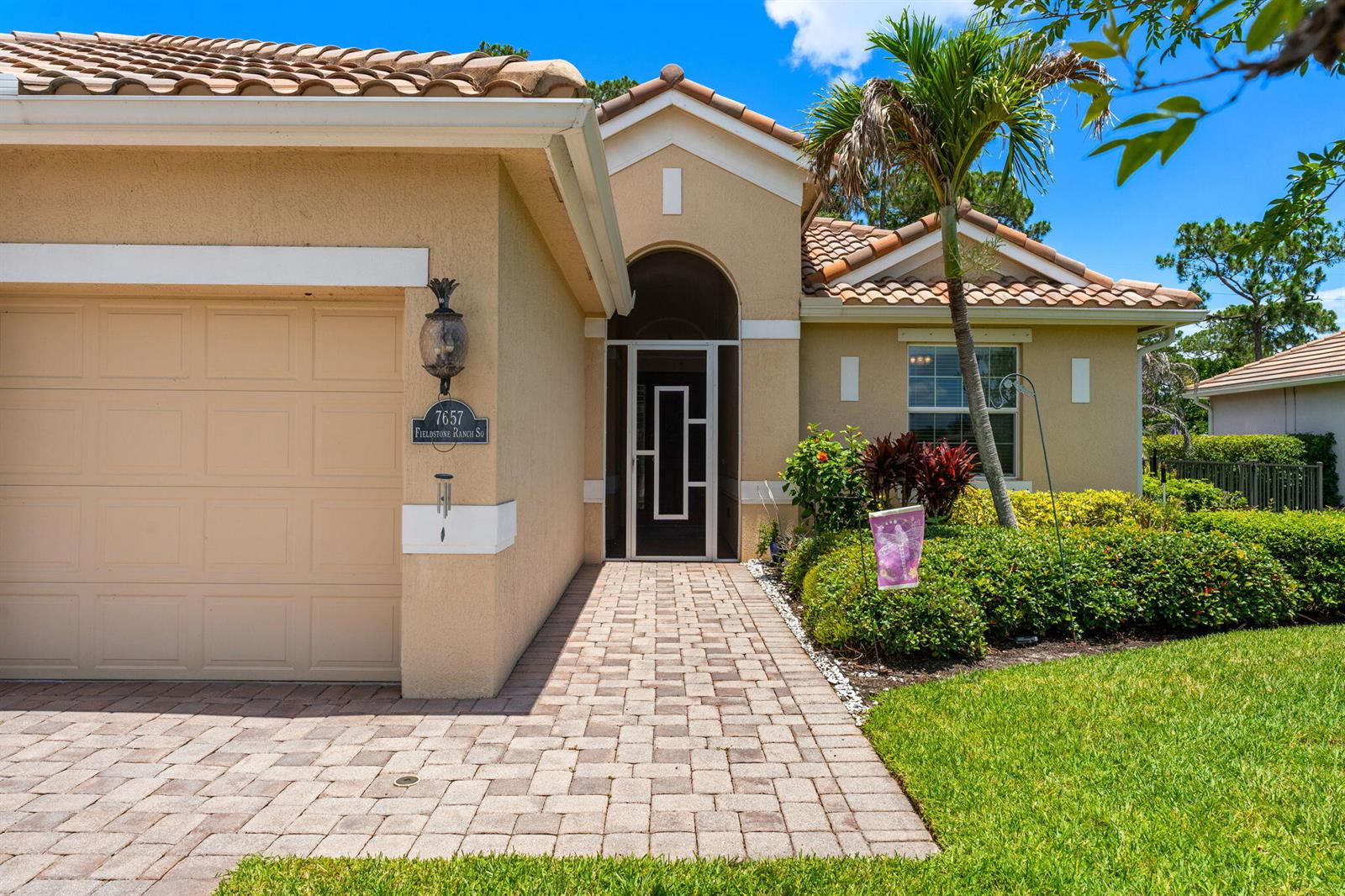 The exterior of a beige house features a tiled roof, a paved walkway, and a garage — 7657 Fieldstone Ranch Square, Vero Beach FL 32967, VERO BEACH, FL