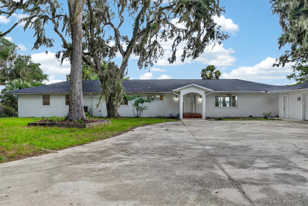 A single-story house with a white exterior, a dark roof, and a large concrete driveway — 157 W GRANDVIEW DRIVE, EAST PALATKA, FL
