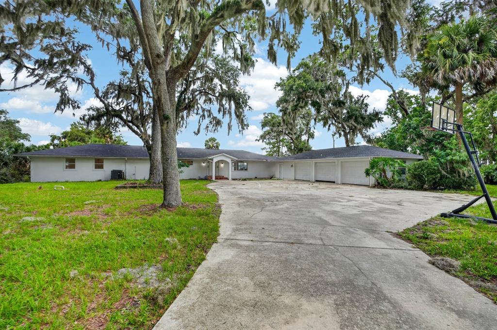A single-story house with a three-car garage, a large concrete driveway, and mature oak trees — 157 W GRANDVIEW DRIVE, EAST PALATKA, FL