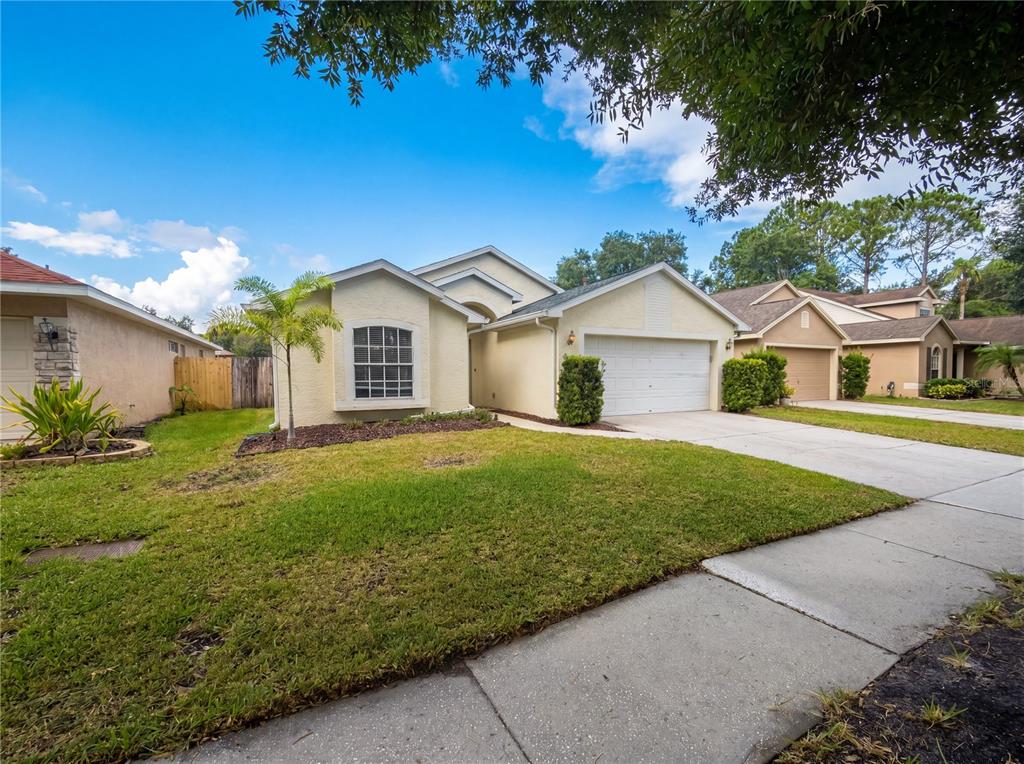 A single-story suburban house with a beige stucco exterior, a two-car garage, and a lawn — 4532 PERDITA LANE, LUTZ, FL