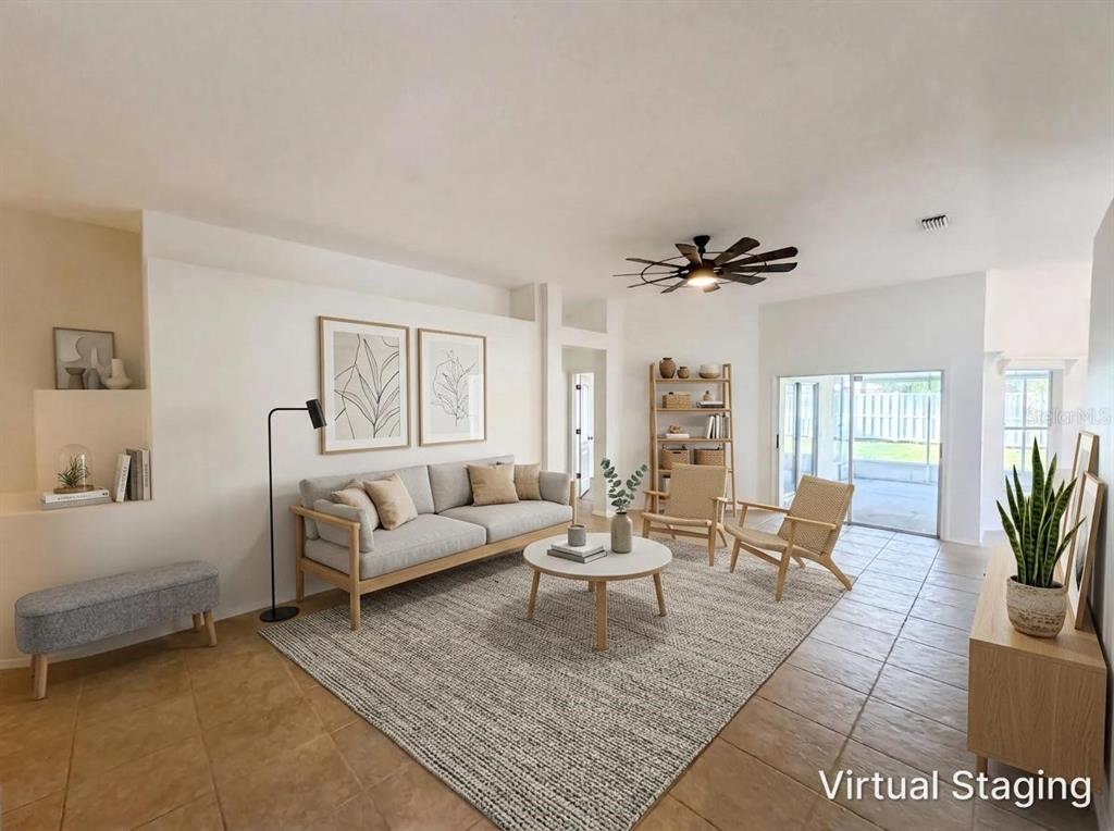 A living room with tile floors, a gray sofa, two wooden chairs, and a ceiling fan — 4532 PERDITA LANE, LUTZ, FL
