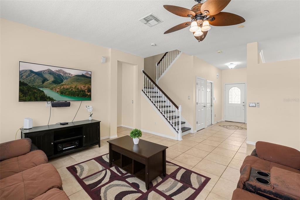 A living room features tile flooring, a staircase, a ceiling fan, and a wall-mounted television — 1573 ANNA CATHERINE DRIVE, ORLANDO, FL