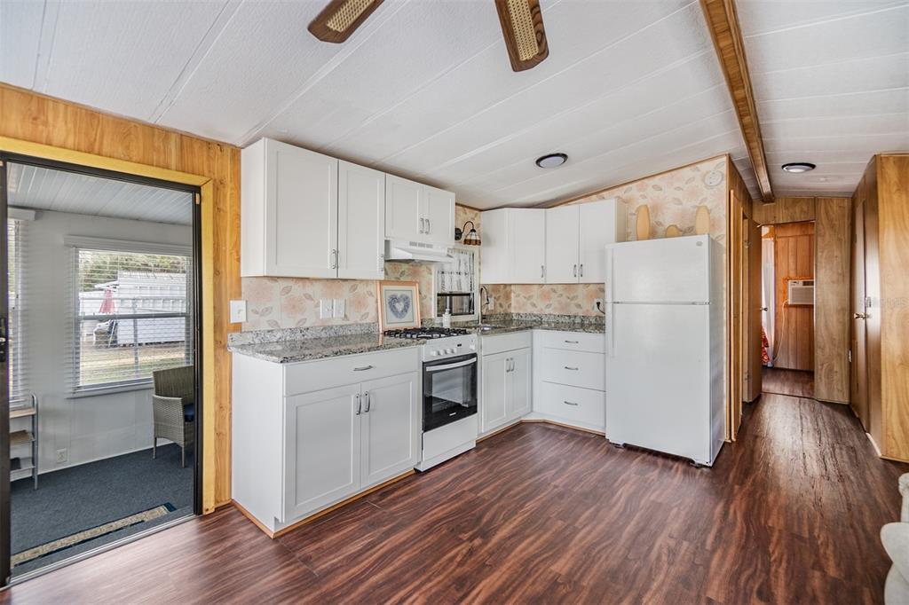 A kitchen features white cabinets, granite countertops, a white refrigerator, and wood-look flooring — 39334 MAHER DRIVE, ZEPHYRHILLS, FL