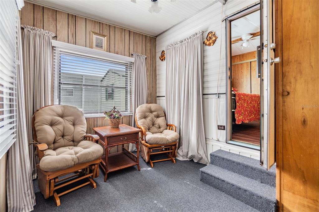 A sunroom features wood-paneled walls, two cushioned rocking chairs, a side table, and carpeted flooring — 39334 MAHER DRIVE, ZEPHYRHILLS, FL
