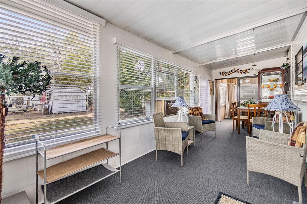 A sunroom features gray carpeting, wicker chairs, and large windows overlooking a backyard shed — 39334 MAHER DRIVE, ZEPHYRHILLS, FL