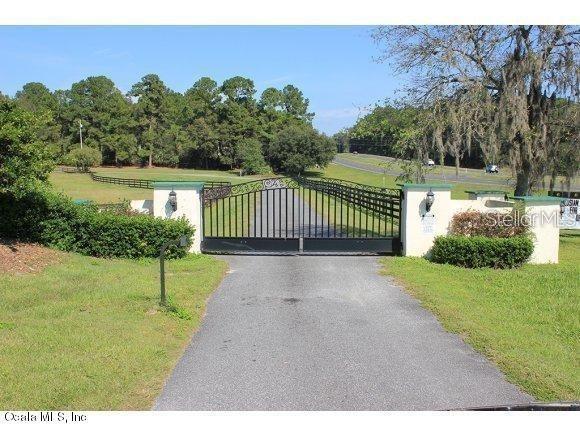 A black metal gate stands between two white stucco pillars at the entrance of a driveway — 12020 N US HIGHWAY 441, OCALA, FL