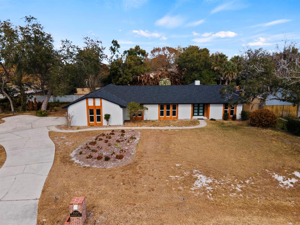 An exterior view of a single-story white house with a dark roof and wood-trimmed windows — 7337 BRANCHTREE DRIVE, ORLANDO, FL
