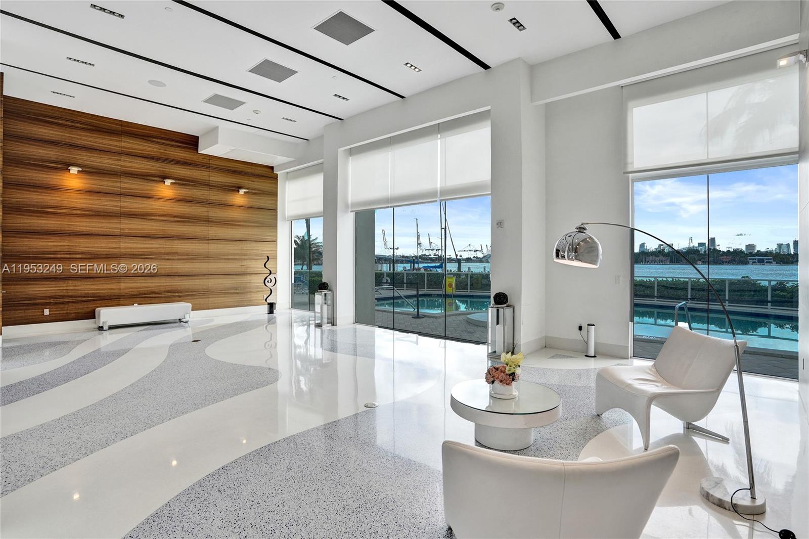 A modern lobby features a wood-paneled wall, patterned flooring, and floor-to-ceiling windows overlooking a pool — 650 West Ave # 2206, Miami Beach FL 33139, MIAMI BEACH, FL