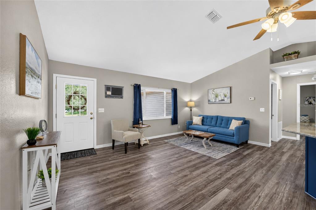 A living room features wood-look flooring, a blue sofa, a white front door, and vaulted ceilings — 13685 SE 90TH COURT, SUMMERFIELD, FL