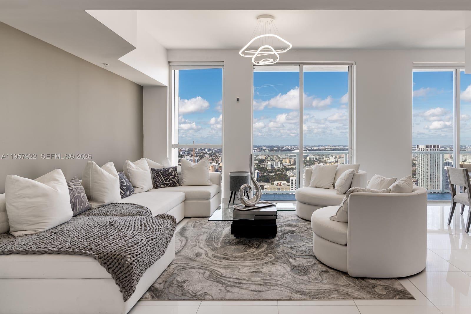 A modern living room features white furniture, a patterned area rug, and floor-to-ceiling windows — 253 NE 2nd St # 4904, Miami FL 33132, MIAMI, FL