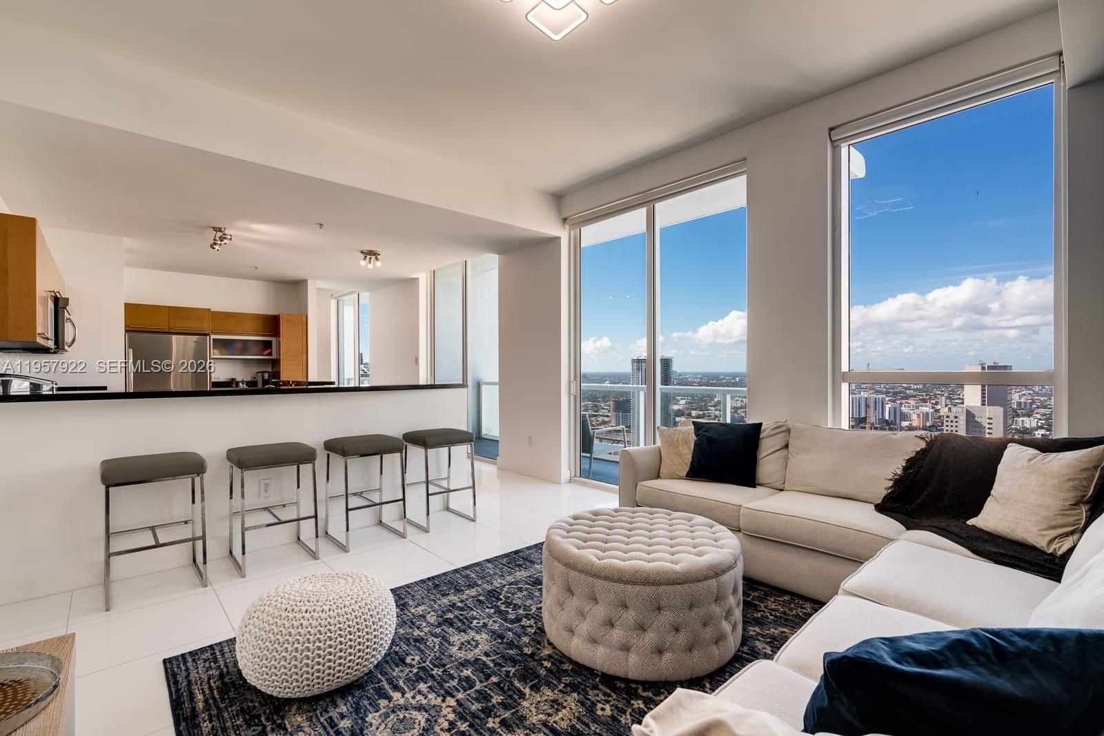 A modern living room with a kitchen bar, white tile floors, and floor-to-ceiling city views — 253 NE 2nd St # 4904, Miami FL 33132, MIAMI, FL