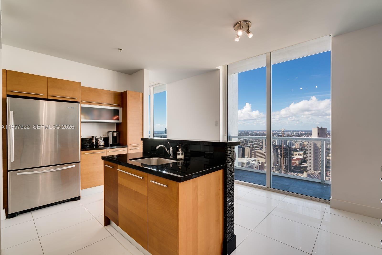 A modern kitchen features wood cabinets, black countertops, and floor-to-ceiling windows with city views — 253 NE 2nd St # 4904, Miami FL 33132, MIAMI, FL