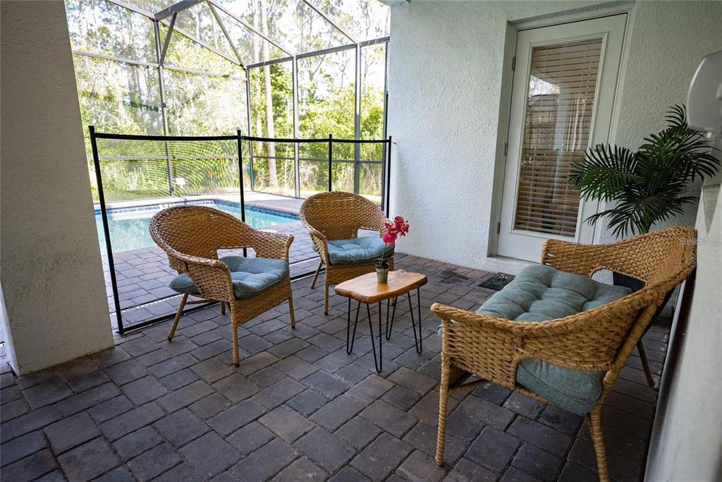 A covered patio features wicker furniture, a small wooden table, and a screened-in swimming pool — 2701 BOOKMARK DRIVE, KISSIMMEE, FL