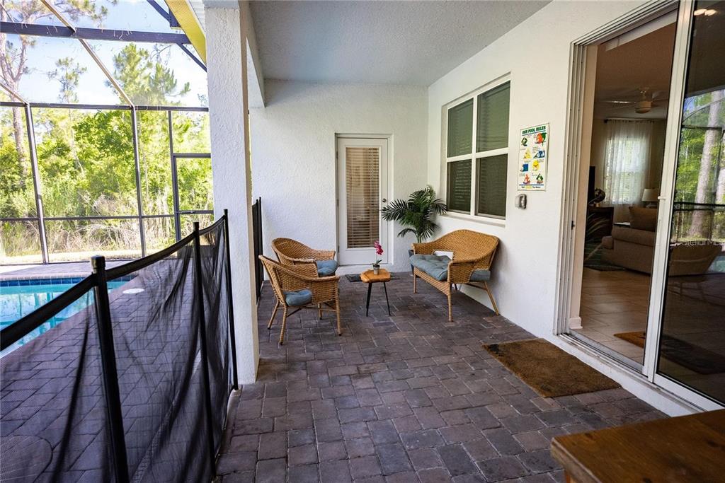 A covered patio features wicker furniture, a pool safety fence, and a view of trees — 2701 BOOKMARK DRIVE, KISSIMMEE, FL