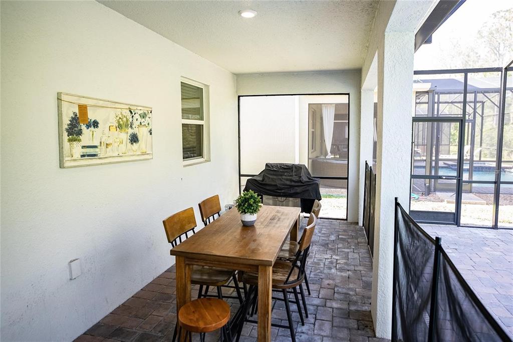 A covered patio features a wooden dining table, a grill, and a screened-in pool area — 2701 BOOKMARK DRIVE, KISSIMMEE, FL