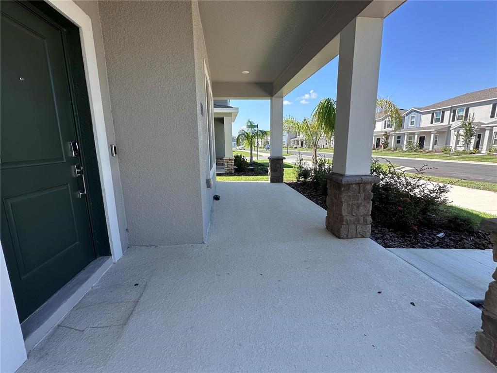 A covered concrete porch features a dark green front door and stone-based support columns — 6110 BLISSFUL STREET, CLERMONT, FL