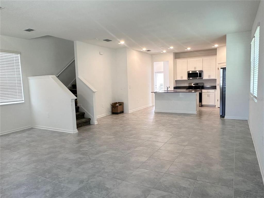 An open-concept living area with tile flooring, a staircase, and a kitchen with white cabinets — 6110 BLISSFUL STREET, CLERMONT, FL
