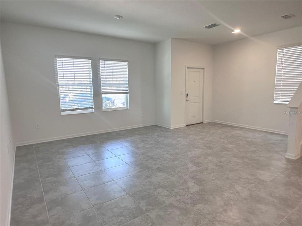 A bright, empty room features light gray tile flooring, white walls, and several windows — 6110 BLISSFUL STREET, CLERMONT, FL